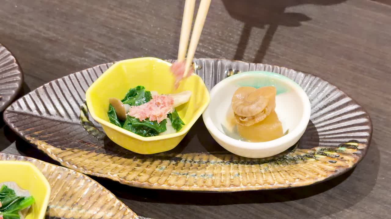 東京で装飾的な陶器の皿からほうれん草を箸でつまむクローズアップショット