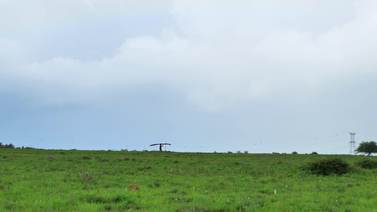 한 남자가 멀리서 들판을 지나서 머리에 재료를 들고 있다