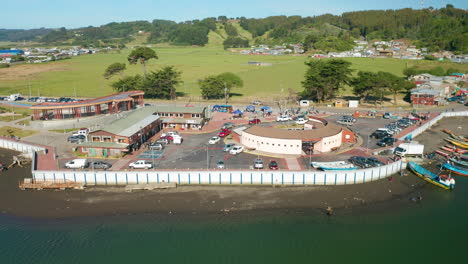 Aerial-truck-shot-of-buildings-and-boat-on-the-coastline-of-Puerto-Saavedra,-Araucania,-Chile,-bright-sunny-day