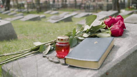 close up view of red roses, bible and candle on tombstone in a gravevard