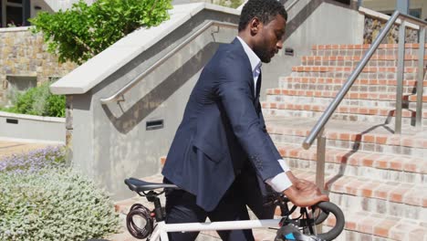 happy african american businessman going up stairs with bike, slow motion