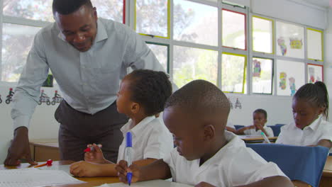 Teacher-stands-helping-elementary-school-kids-at-their-desks