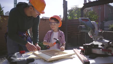 the father teaching his son to use hammer and nails