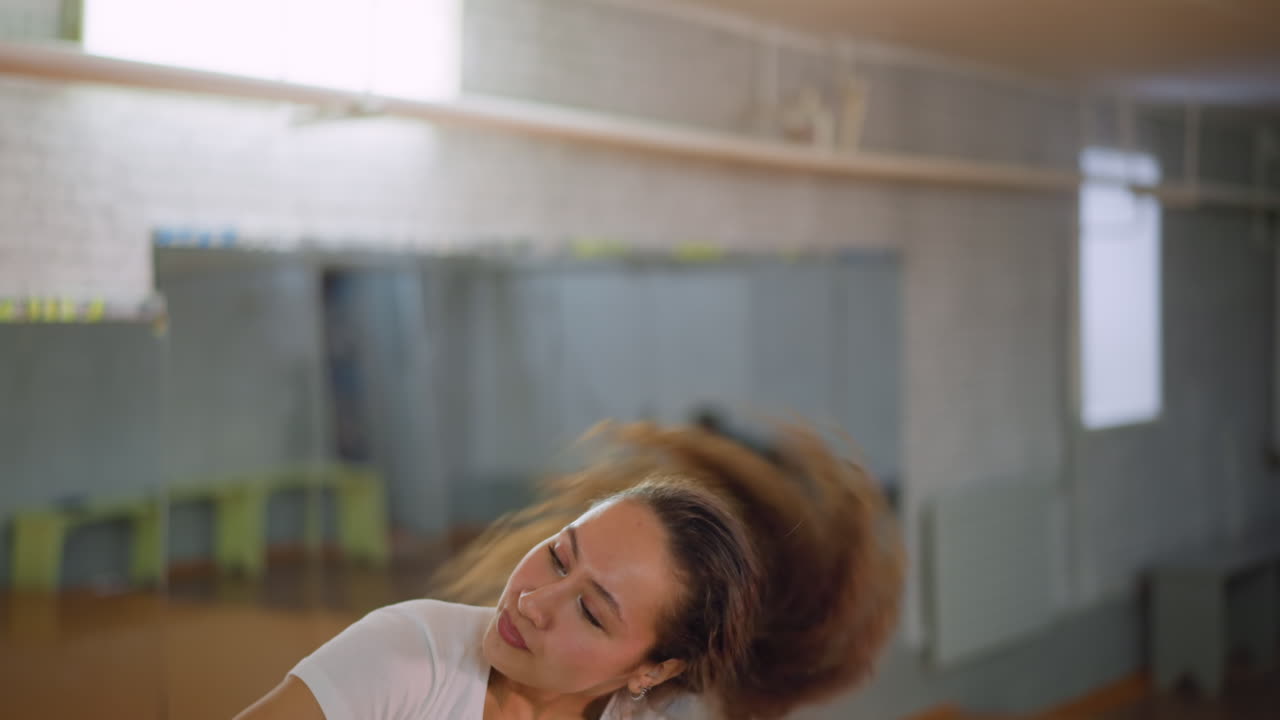 Side view of lady in white top flipping hands during expressive workout in fitness studio, showing rhythm, energy, and graceful controlled motion with focus and determination