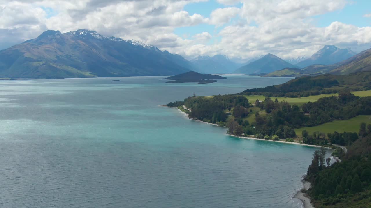 Drone footage of a blue lake in New Zealand with mountains in the distance