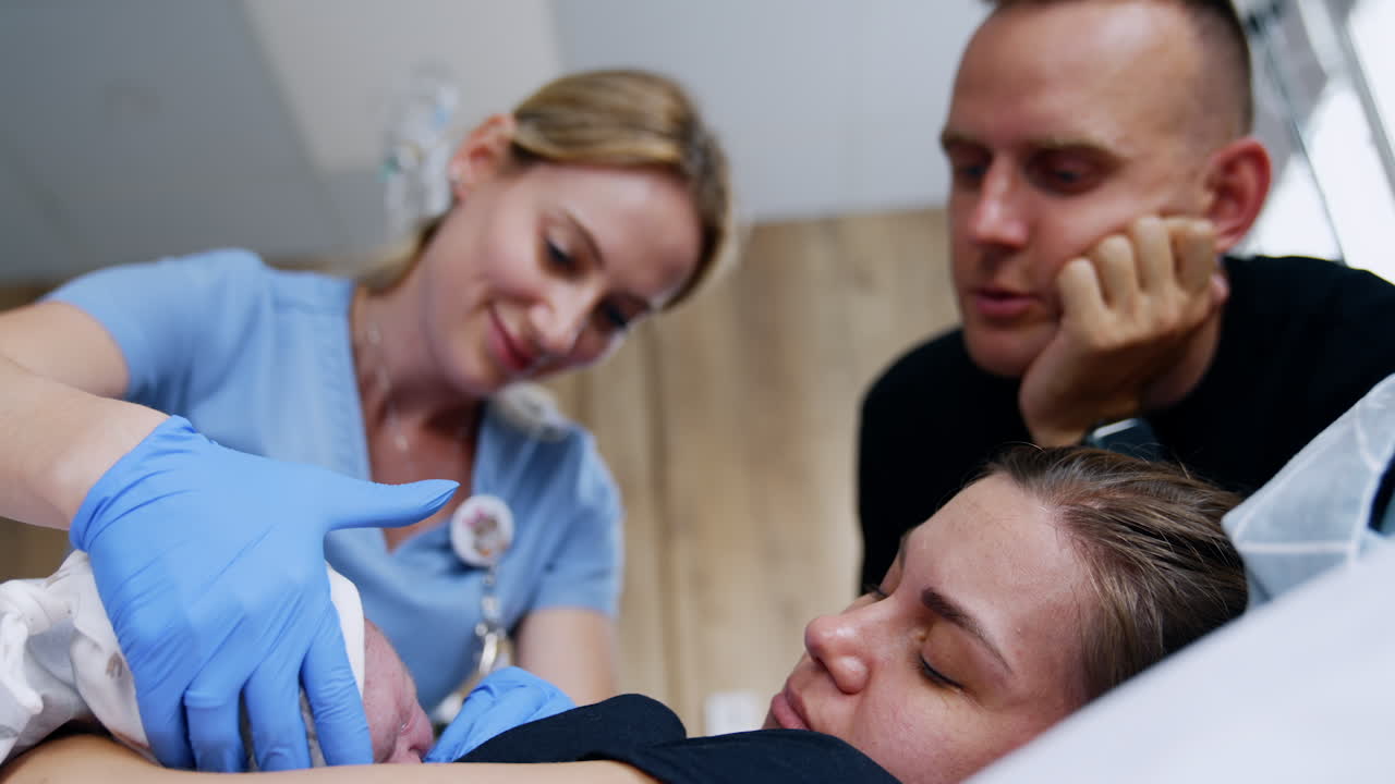 Female breastfeeding consultant helping a newborn to take mom's breast. Happy father is watching the process. Low angle view.