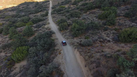 Aerial-drone-flying-above-fast-red-Jeep-driving-on-off-road-trail,-forward