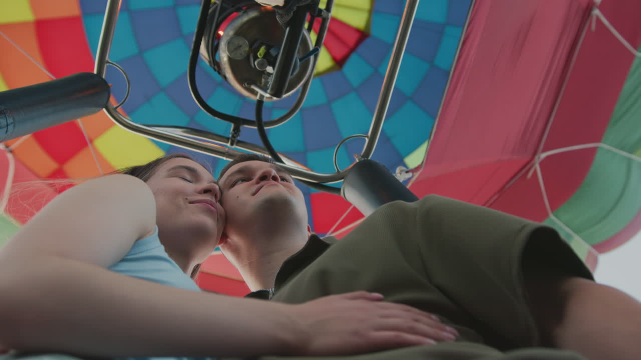 Low angle view of romantic couple hugging while enjoying peaceful moment inside vibrant hot air balloon, surrounded by colorful panels and open sky, pair shares connection