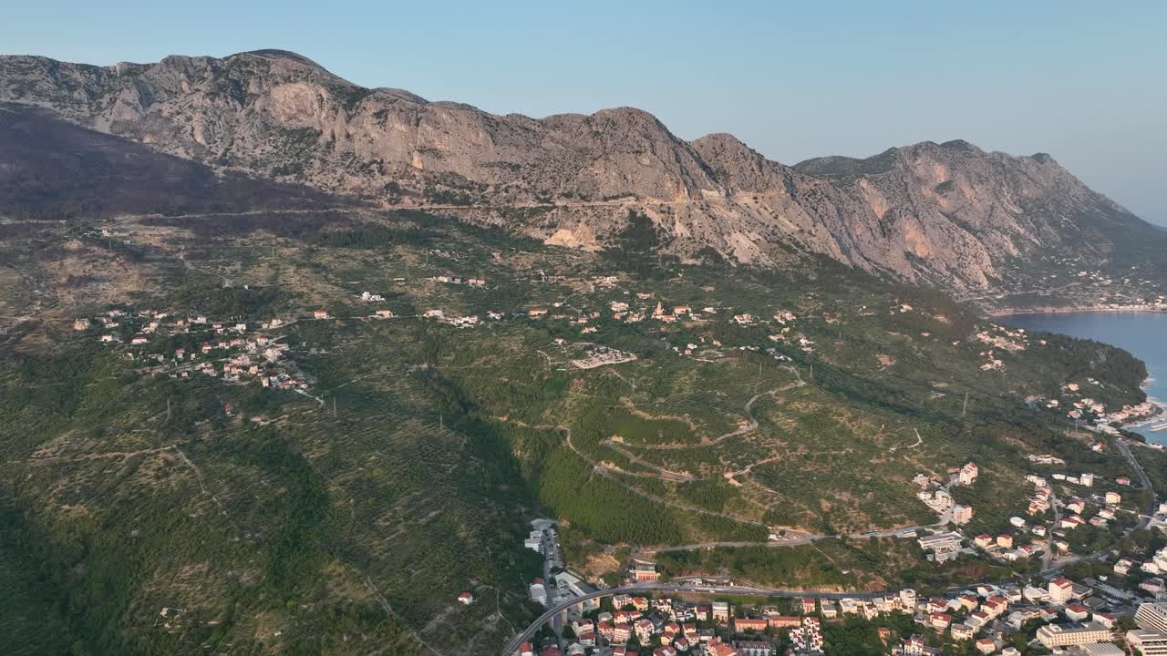 Aerial turns from Biokovo mountains to top down view of Podgora harbor, beach, and promenade at sunset