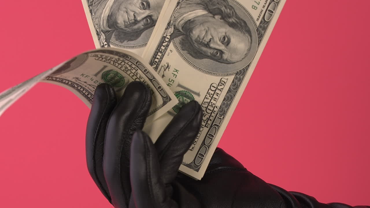 Handskebeklædt hånd spreder amerikanske hundrede-dollarsedler ud