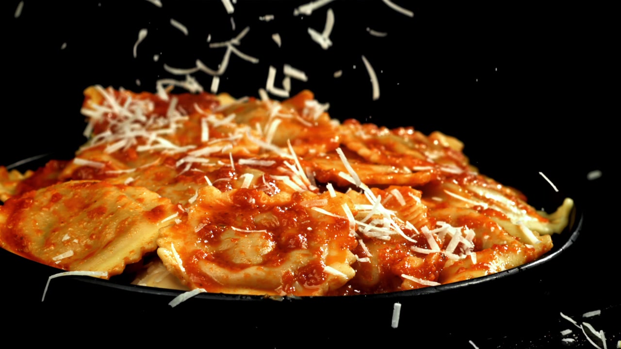 Parmigiano grattugiato che cade su deliziosi ravioli con salsa di pomodoro