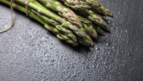 raw green asparagus on wet black slate background. rotating