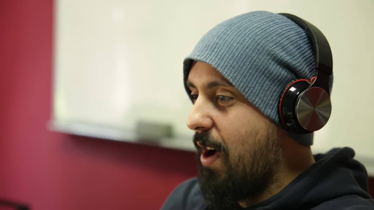 Giovane uomo barbuto ed elegante che ascolta musica con cuffie wireless, scuotendo la testa e seguendo il ritmo della canzone
