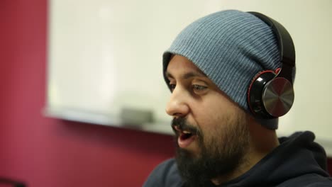 young bearded stylish man listening music by wireless headphones, shaking his head, following the song rhythm