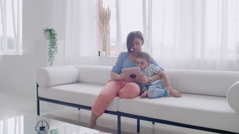 madre e hijo usando tableta mirando la pantalla y hablando en el sofá en una casa acogedora