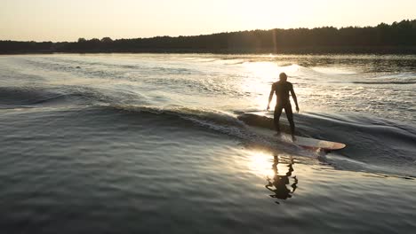 surfista en una ola de surf longboard detrás de un barco con un paso cruzado al atardecer