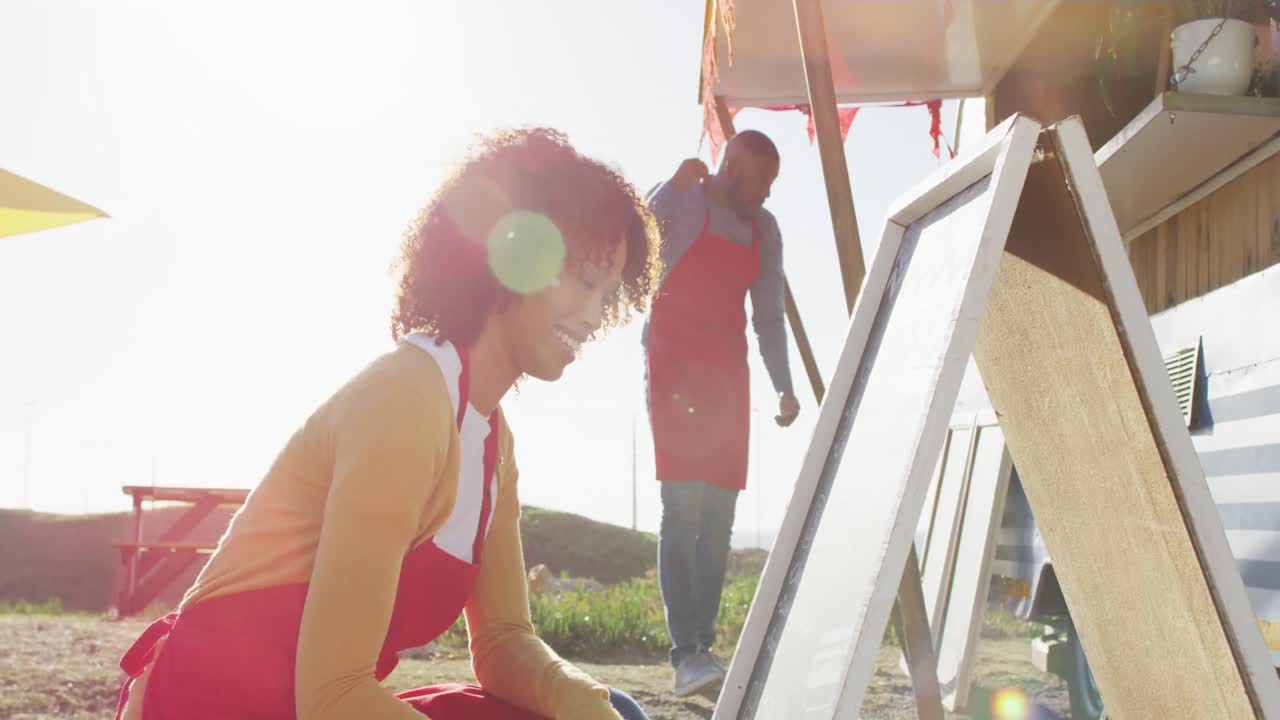 mujer afroamericana con delantal escribiendo en el menú de alimentos de la pizarra del camión de alimentos
