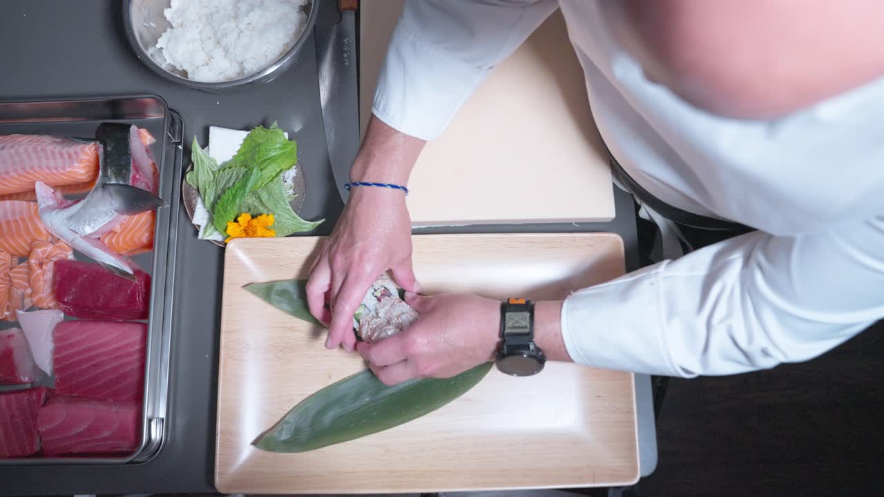 A static overhead shot showing sushi being carefully arranged and placed into a decorative bowl, emphasizing presentation and culinary artistry.