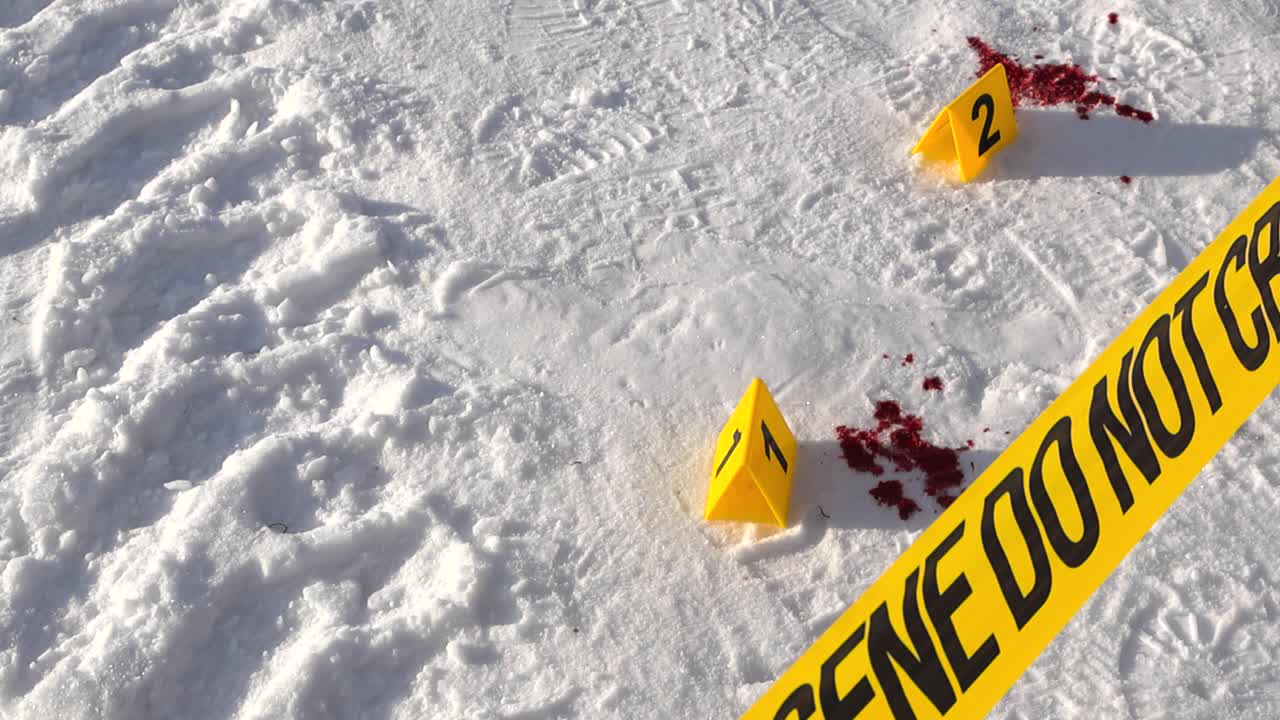 Downward view over forensic ribbon toward numbered markers and red stains on winter ground