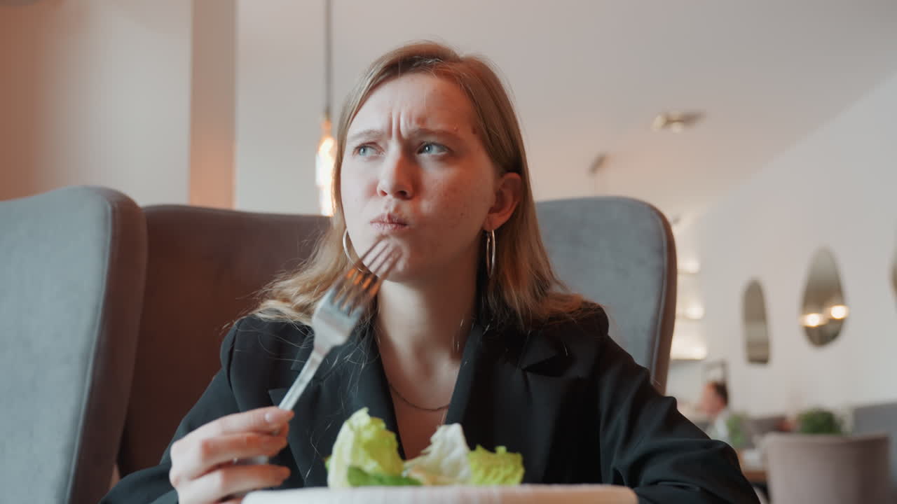 Caucasian woman in cafe grimacing at salad, business attire, fork held ...