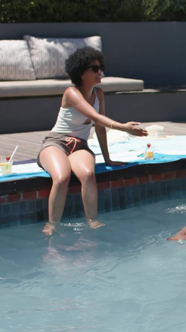 Vertical video: Reaching friend leading seated woman taking drink at home pool, tank-top, donut