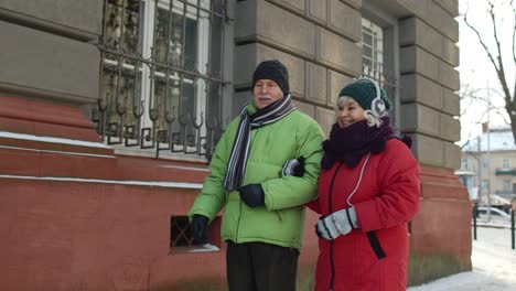 Senior-couple-man,-woman-tourists-walking-in-old-city-in-winter-talking,-gesturing-holidays-vacation