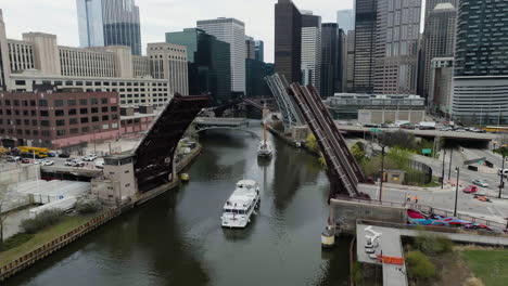 Vista-Aérea-De-Barcos-Que-Se-Mueven-Bajo-Puentes-Elevados-En-El-Río-Chicago,-Primavera-En-Estados-Unidos