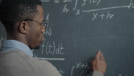 man writing equations on a chalkboard
