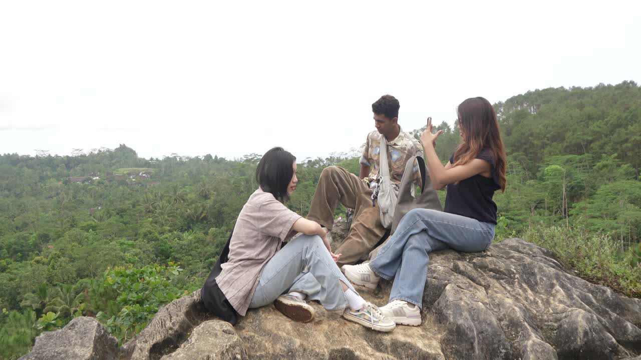 Asian Indonesian Friends Taking Selfies on Mountain Rock with Scenic Forest Background