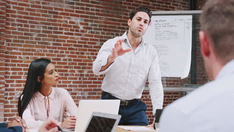 mature businessman standing and leading office meeting around table