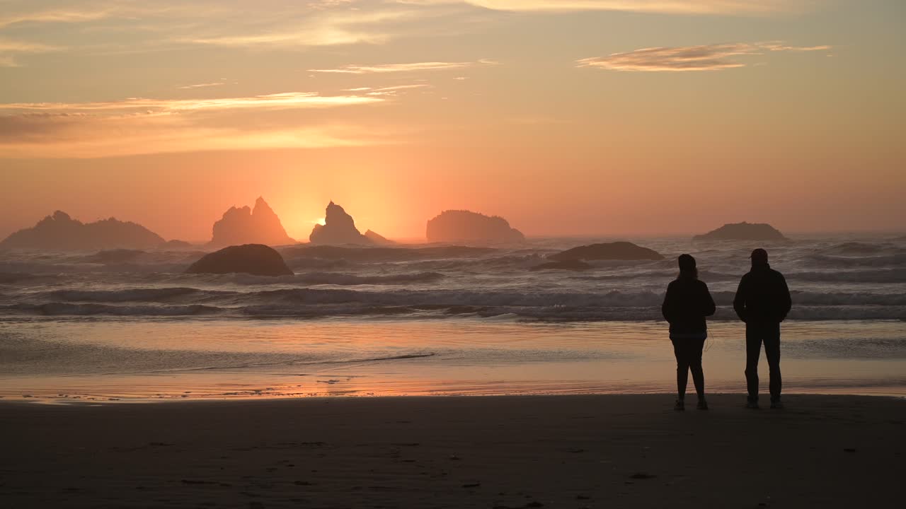Silhouetted couple watches colorful sunset in Bandon Beach, Oregon Coast, USA