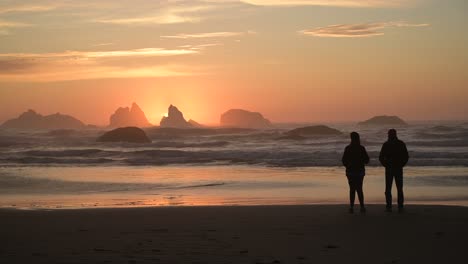 silhouetted couple watches colorful sunset in bandon beach, oregon coast, usa