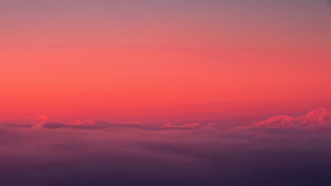 Rising sun causing cloud layer shifting colors at aerial vantage, with horizon line and purple sky
