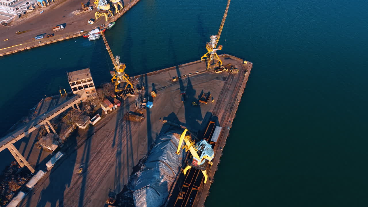 Port pier with cranes and cargo. Top down perspective of industrial harbor activity and storage piles