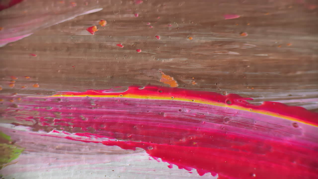 Colorful close up of an abstract painting showing thick brushstrokes in red, pink, yellow, and orange hues