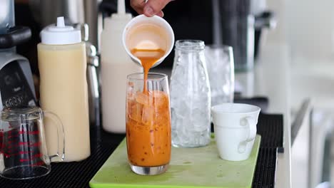 pouring milk into thai tea over ice