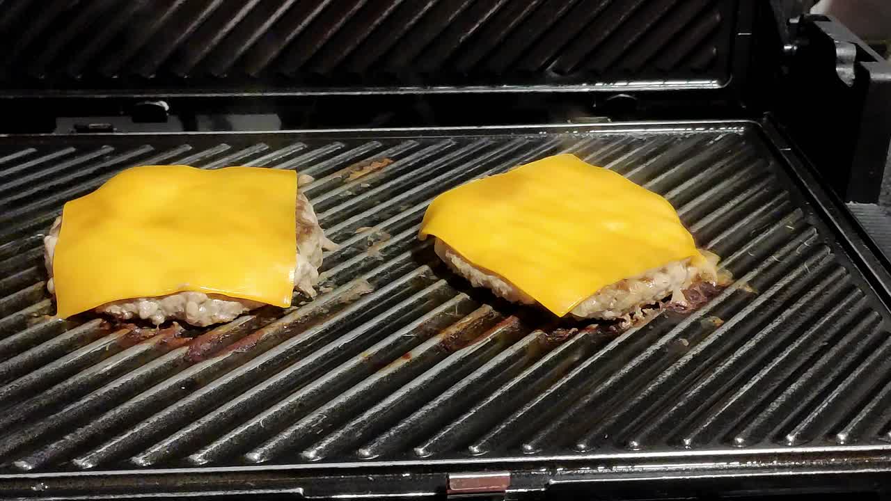 due cheeseburger fatti in casa che cucinano su una griglia nera