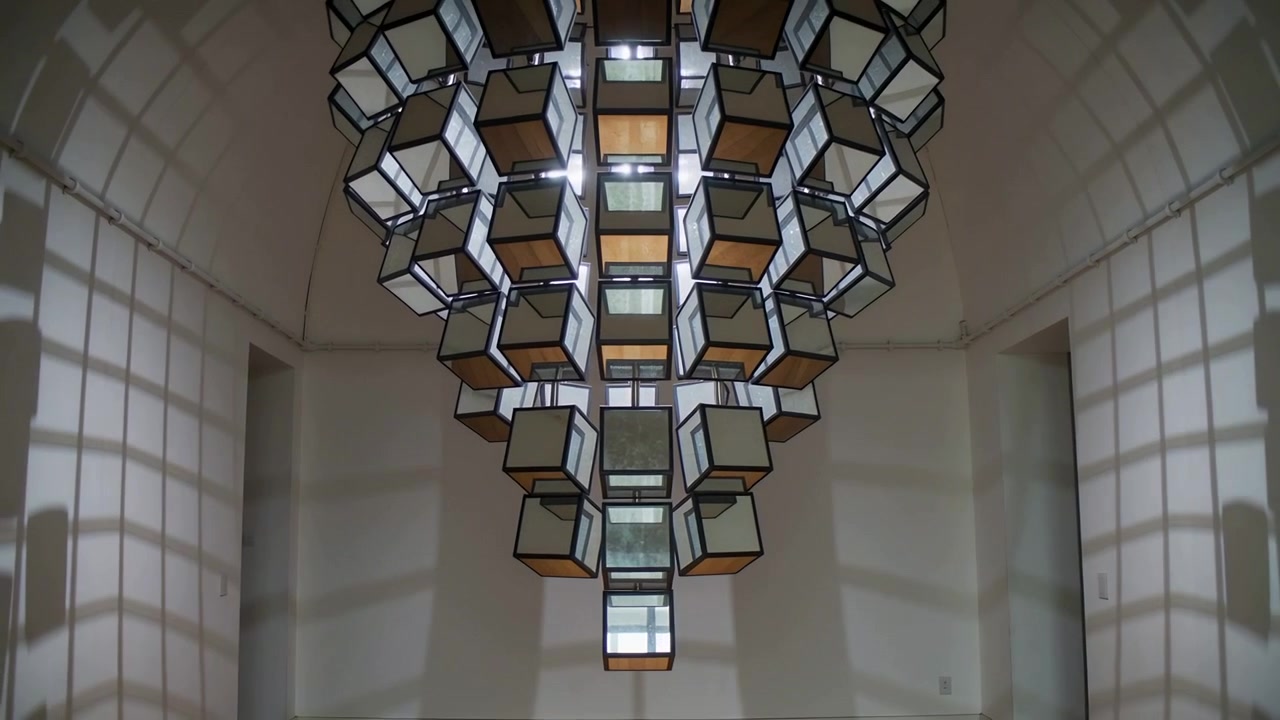 Pouring light via grid panes creating shifting shadows, suspended cube artwork rotating in gallery