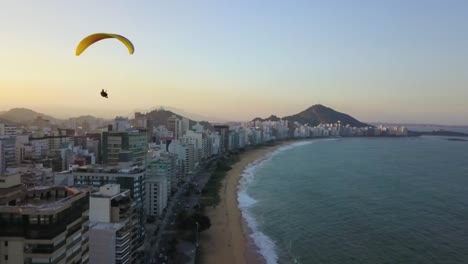 paragliding over the buildings and besides the sea at praia da costa, vila velha, brasil. drone shot.
