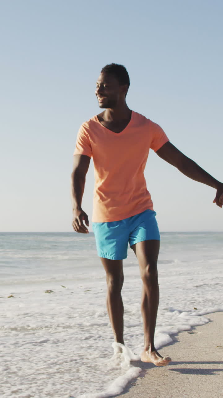 Smiling african american couple holding hands and walking on sunny beach