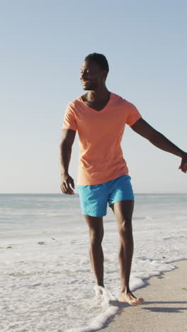 smiling african american couple holding hands and walking on sunny beach