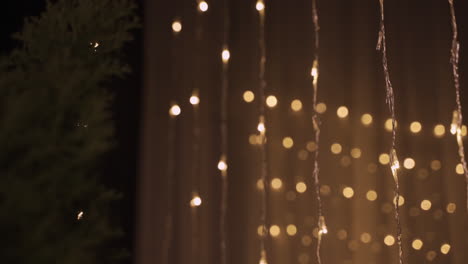 camera focuses on garlands of golden christmas lights in dark party room decorated with christmas tree 3