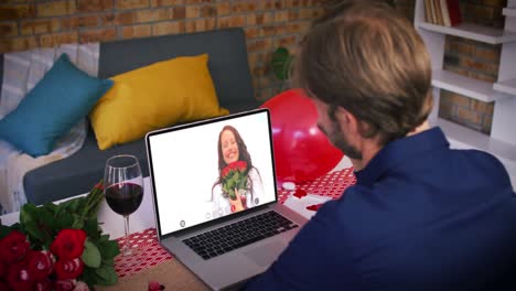 Caucasian-couple-on-a-valentines-date-video-call-man-waving-to-smiling-woman-holding-red-roses-on-la