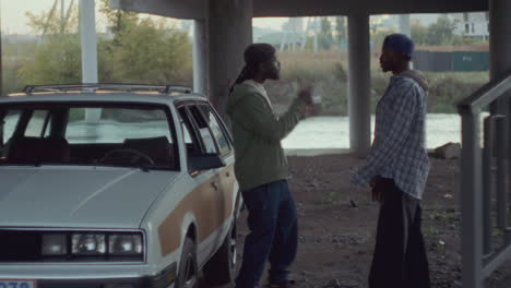 two black men having heated argument in gritty urban area under overpass