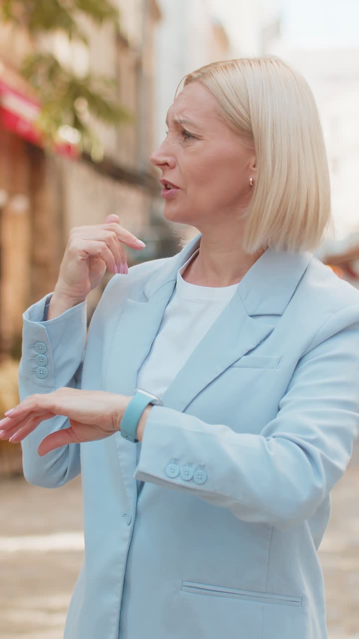 Shocked mature woman businesswoman in hurry checking time on smartwatch walking on city street