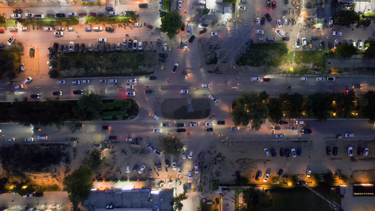 Aerial drone shot straight down into busy roundabout turn with cars passing slowly and being parked at the shopping complexes houses and offices nearby