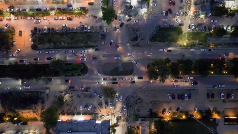 aerial drone shot straight down into busy roundabout turn with cars passing slowly and being parked at the shopping complexes houses and offices nearby