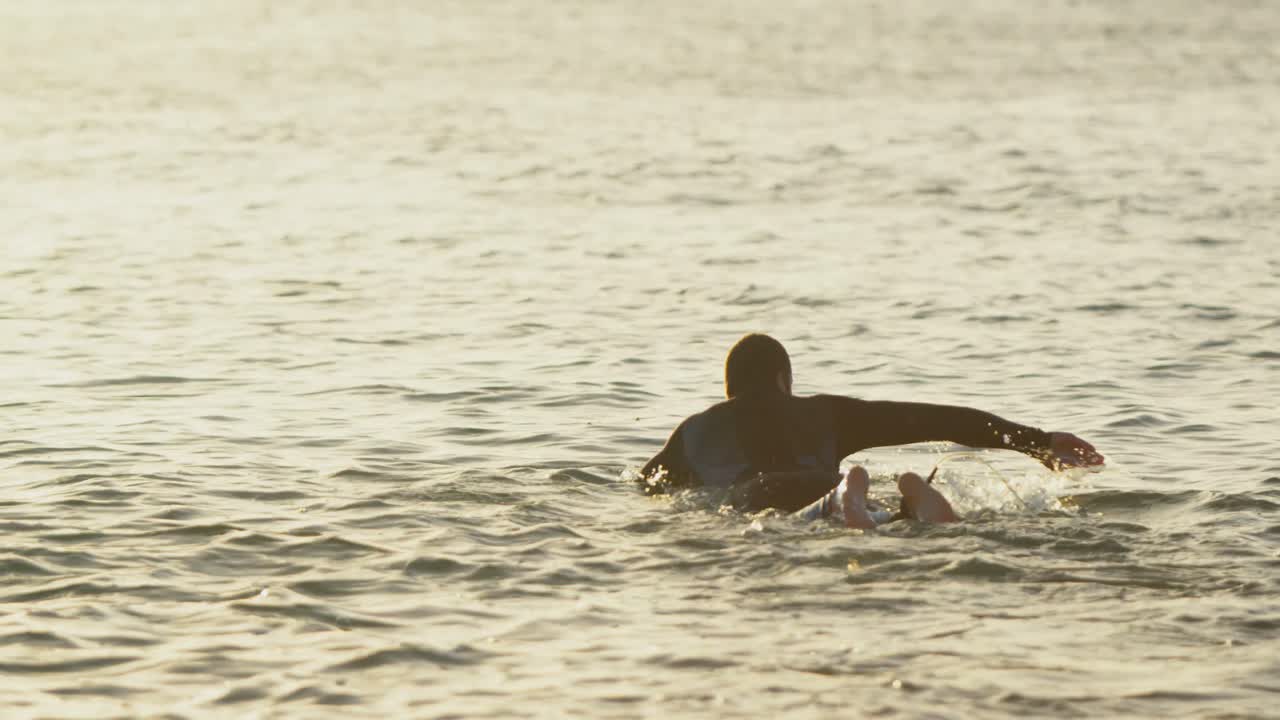 vista trasera de un surfista caucásico adulto nadando en el mar durante la puesta de sol 4k
