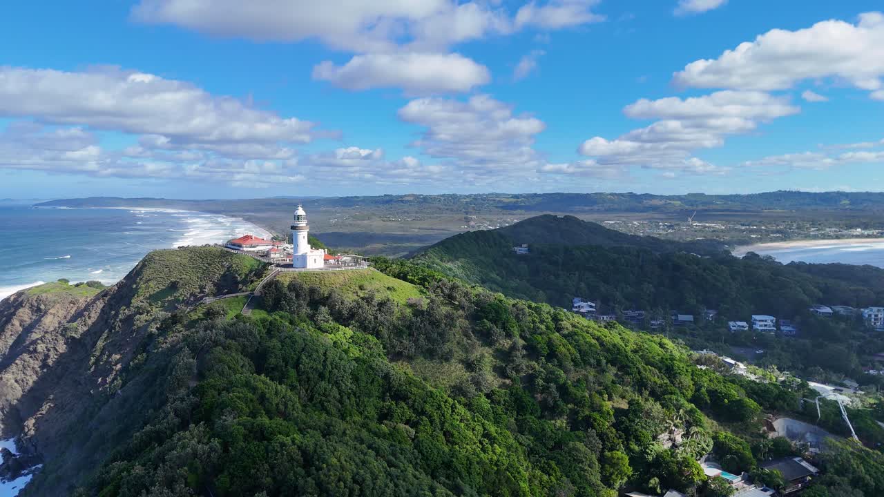 Aerial footage captures Byron Bay lighthouse, lush greenery, and coastline under clear skies with dynamic camera movement