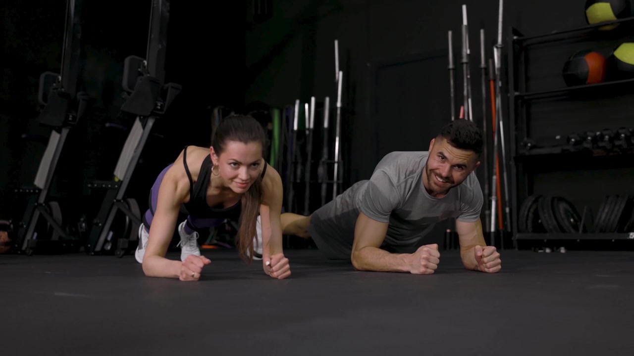 Pareja en forma haciendo el ejercicio de la plancha juntos en un gimnasio moderno